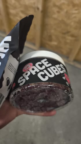 Ein Kunde hält einen durchsichtigen Behälter voller THC Space Cubes neben der Verpackung.