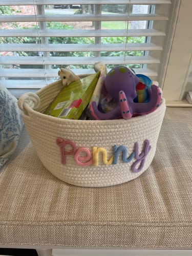 Customer's personalized woven basket with the name 'Penny' in colorful letters, filled with toys.