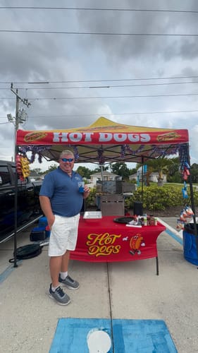 Customer wearing the white patterned Hitting Jackpots Golf Shorts outdoors by a hot dog stand.