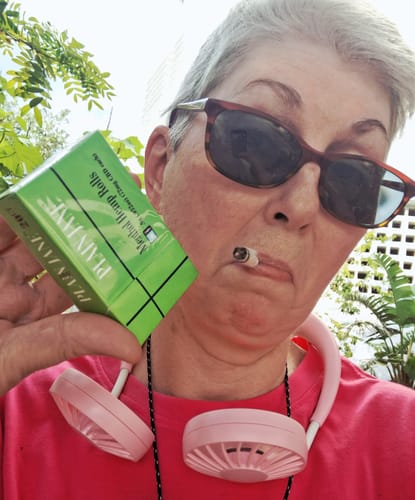 Customer poses outdoors with a box of Menthol Filtered Hemp Pre-Rolls and one in their mouth.