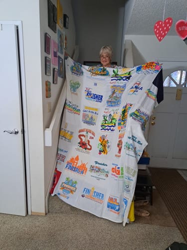 Customer holding up a large Premium T Shirt Quilt made from many light-colored and colorful t-shirts.