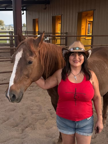 Customer in a cowboy hat smiling while standing next to a brown horse in a stable.