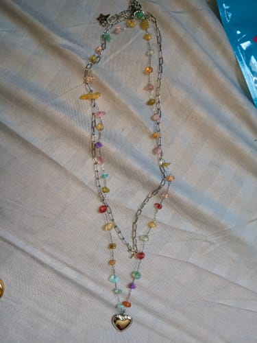 Reseñador mostrando el Collar Iris Plata completo sobre una superficie clara, con cuentas de colores y un colgante de corazón.