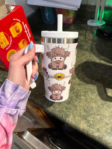 Reviewer's hand holding the patterned Highland Cow Kids CREWCUP, showing the handle and spill-proof lid.