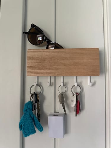Kundens hvite, magnetiske nøkkelholder montert på en vegg, med nøkler og solbriller.