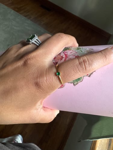 Reviewer wearing the dainty gold Birthstone Ring with a green stone on one finger, next to a silver ring on another.