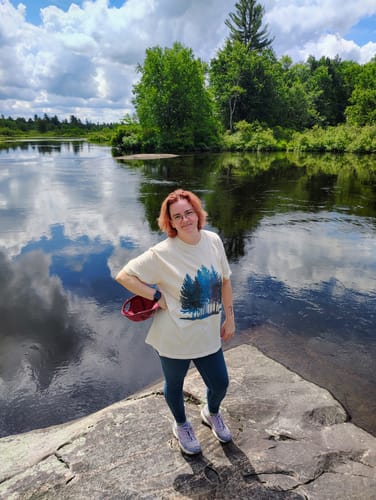 Reviewer wearing the relaxed-fit Water Color Forest T-shirt while standing on a rock by a river.