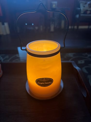 Customer's Pumpkin Pancakes Candle lit and glowing warmly inside a decorative metal holder on a table.