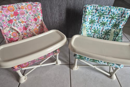 Reviewer's two Paloma baby chairs, one with a bright floral print and the other with a palm tree pattern, set up indoors.