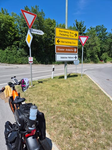 Reviewer's Lankeleisi MG600 Plus e-bike with rear pannier bags parked at a crossroads with multiple direction signs.