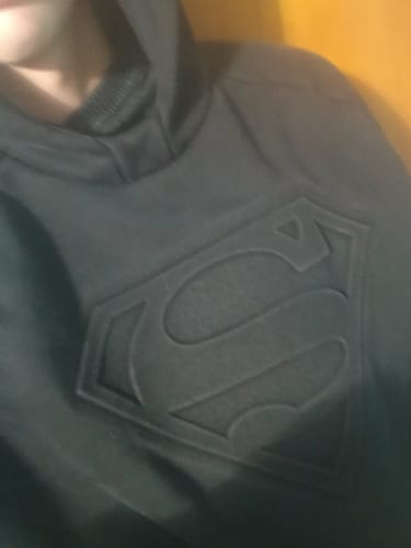A close-up of a reviewer wearing the dark Superman Shield Hoodie, showing the embossed logo on the chest.