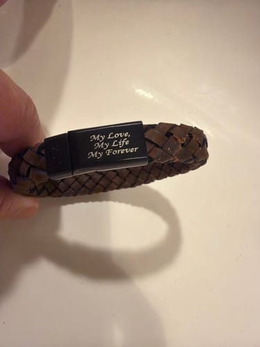 Customer holding a brown leather bracelet with a black clasp engraved with 'My Love, My Life, My Forever'.