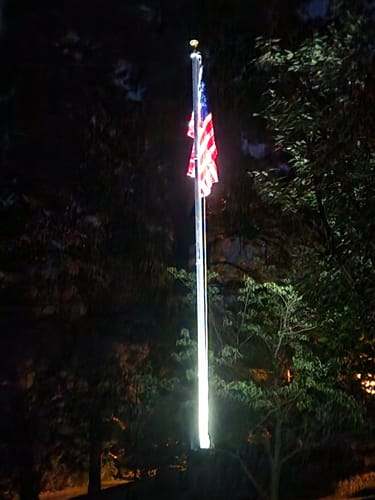 Customer's Solar Powered Flagpole Triple Uplight brightly illuminating a tall flagpole with an American flag at night.