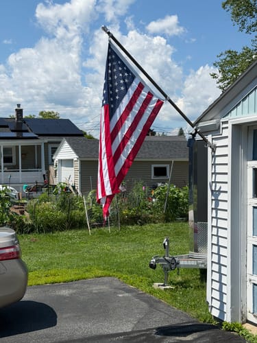 Customer's Prestige House Flag Pole mounted on a garage, displaying the American flag on a sunny day.