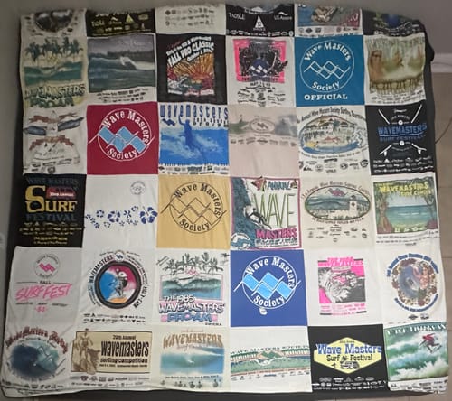 Reviewer's large T-Shirt Quilt made from colorful, vintage surf contest t-shirts spread on a bed.