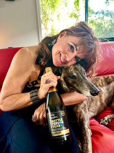 Reviewer smiling on a couch, holding a bottle of Sparkling wine while hugging their dog.