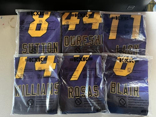 Customer's order of six custom purple basketball jerseys with yellow lettering, shown folded in clear packaging.