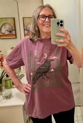 Reviewer smiling in a mirror selfie, wearing the mauve Raven Bough T-Shirt.