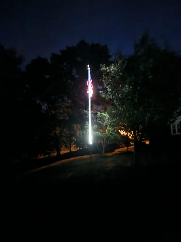 Reviewer's Solar Powered Flagpole Triple Uplight lighting up a flagpole with an American flag in a yard at night.