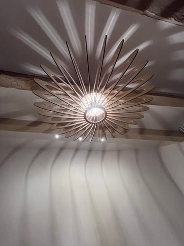 Photo d'un client de la suspension NEO allumée, projetant un jeu d'ombres élégant sur le plafond et le mur.