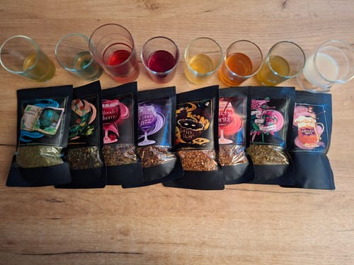Kunde zeigt alle 8 Sorten des Cold Brew Tee Bundles mit den farbenfrohen, zubereiteten Getränken in Gläsern dahinter.
