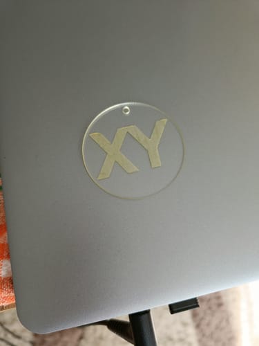 Customer's clear keychain with 'XY' laser engraved, shown on a silver laptop.