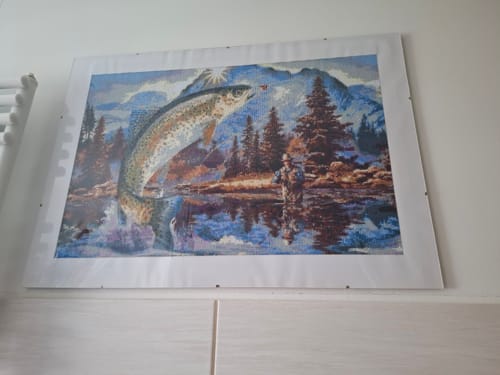 Kunde zeigt das fertige Diamond-Painting 'Angeln Im Meer', das an einer Wand hängt und einen Fisch in einer Berglandschaft darstellt.