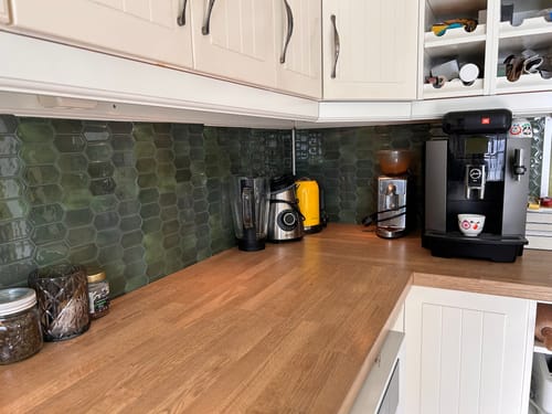 Kundens kjøkken med Alexandra grønne veggfliser som backsplash over en trebenkeplate med hvite overskap.
