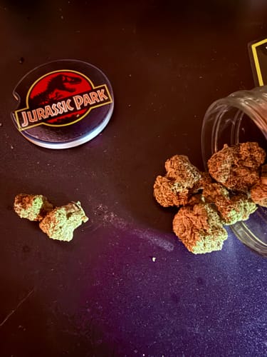 Customer's Biscotti THCA Flower buds spilled from a glass jar onto a dark surface next to a coaster.