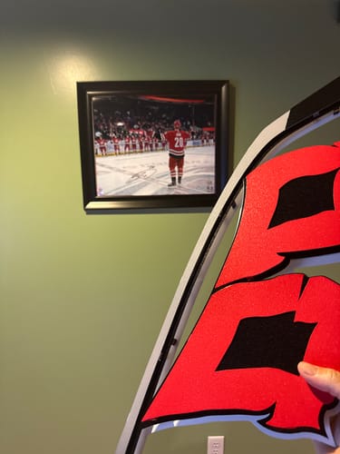 Close-up of a reviewer holding their red Carolina Hurricanes Flag Metal Wall Art before hanging it.