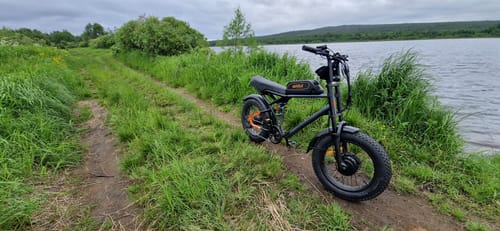 Customer's black Vakole Q20 MAX fat bike parked on a grassy path next to a large body of water.