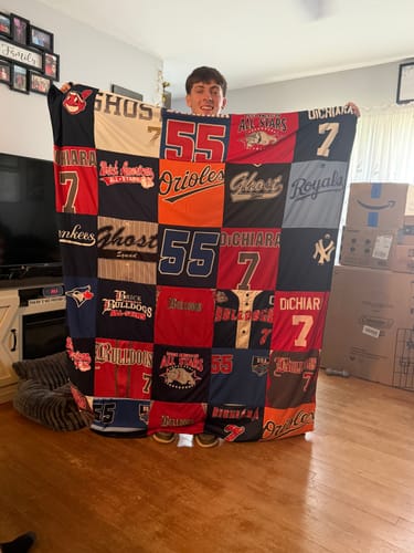 Customer's son holding a large Project Repat T-Shirt Quilt made from colorful baseball jerseys in a living room.
