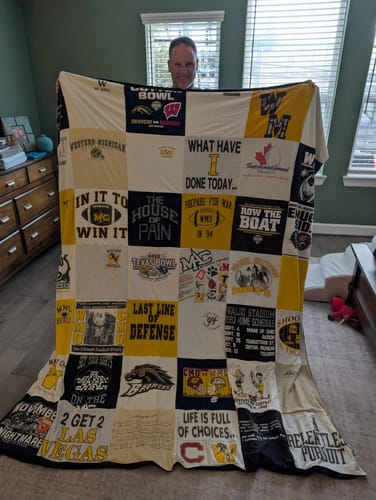 Customer holding up a large Project Repat T-Shirt Quilt made from various yellow, white, and black college t-shirts.