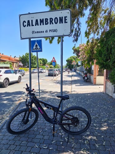 Customer's black Vakole EMT29 e-bike parked on a sunny cobblestone street next to a 'Calambrone' sign.