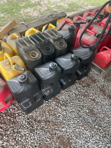 Reviewer's collection of black, yellow, and red gas jugs sitting on gravel, as mentioned for use on a farm.