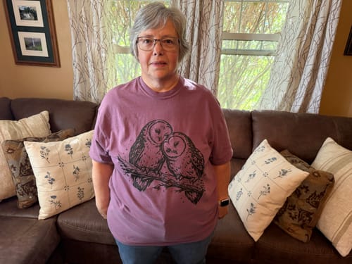 A customer wearing the purple Two Owls T-Shirt while standing in a living room.