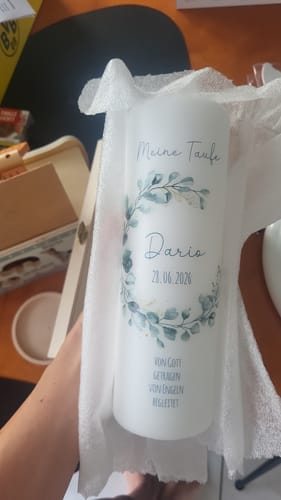 Ein Rezensent hält die personalisierte weiße Taufkerze mit Eukalyptus-Motiv in der Hand.