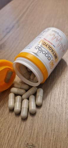 Recensore mostra il flacone di Metaglyc aperto con le capsule sparse su una superficie in legno.