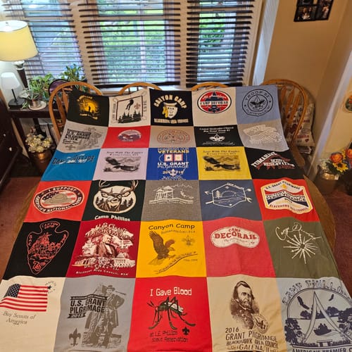 A customer's colorful Project Repat T-Shirt Quilt, made from Boy Scout and event shirts, spread across a table.