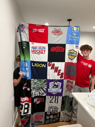 Two customers holding up their large, colorful Project Repat T-Shirt Quilt made from hockey jerseys.