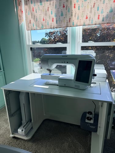 Customer's white Melbourne Sewing Cabinet with a large Brother Luminaire sewing machine set up in a craft room by a window.