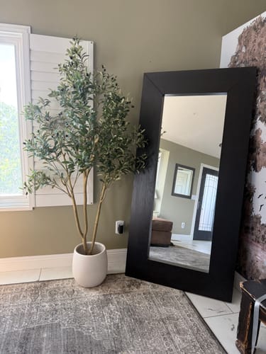 Customer's beautiful Faux Olive Tree in a white pot, shown indoors next to a large, black-framed mirror.