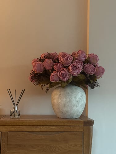 Reviewer's textured, beige Zoe Ceramic Vase holding pink faux roses on a wooden cabinet.