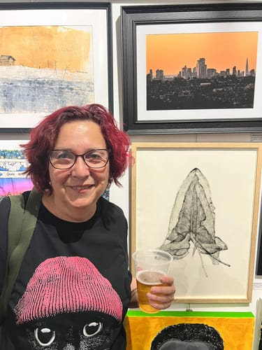 Reviewer at an art show wearing a black t-shirt with the Statement Made Light Pink cat graphic.