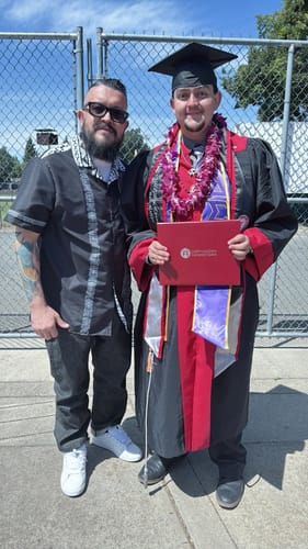 Reviewer proudly wearing the black and white patterned shirt next to a person in a graduation gown.