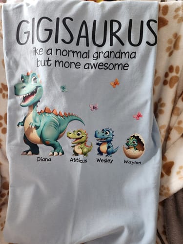 Customer's light blue personalized shirt with 'Gigisaurus ike a normal grandma' text and four cartoon dinosaurs with names underneath.