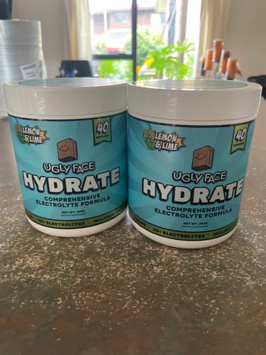 Reviewer's two tubs of UGLYFACE HYDRATE in Lemon & Lime flavor sitting on a counter.
