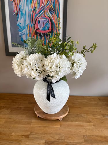 Customer's Faux Eucalyptus & White Hydrangea arrangement in a decorative white vase on a wooden surface.