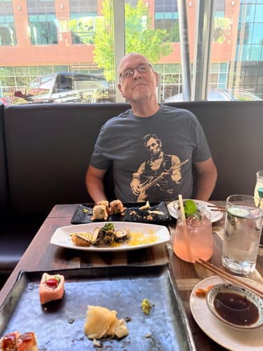 Reviewer wearing the grey Lincoln Guitar T-Shirt while sitting at a restaurant table.