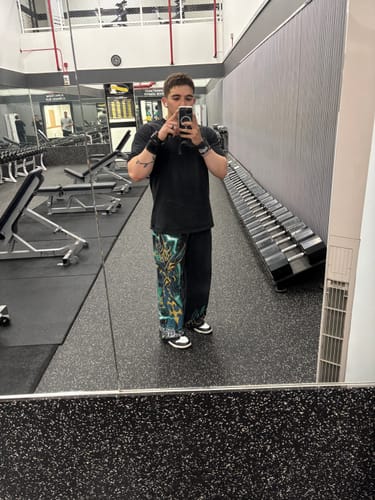 Reviewer in a gym taking a mirror selfie while wearing wide-leg graphic pants and a black t-shirt.